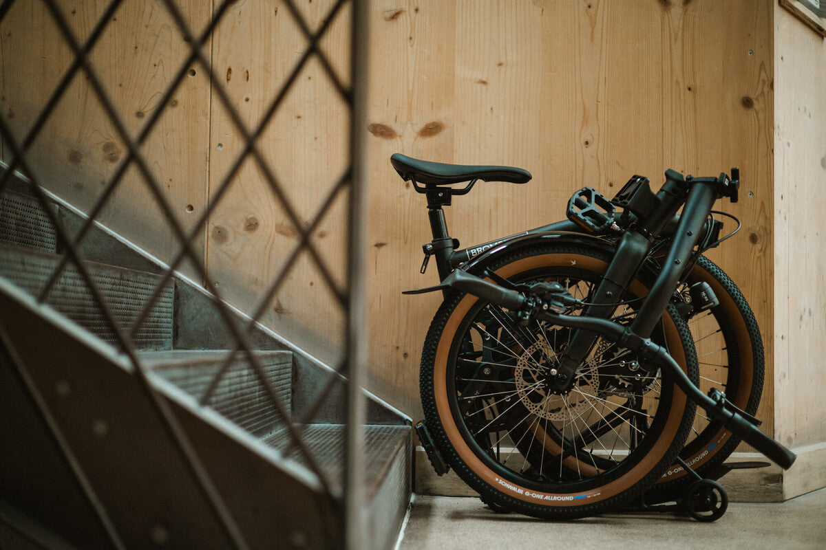 Folded Brompton G Line folding bicycle stored beside a staircase indoors